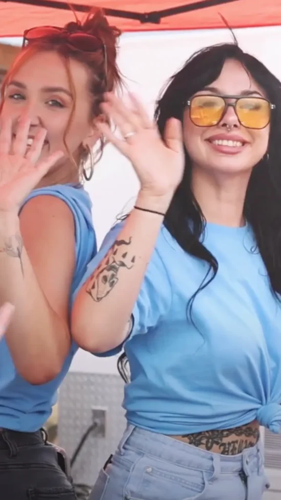 Two smiling women in blue shirts waving.