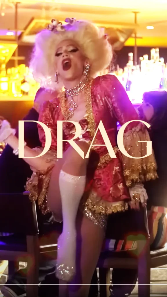 A drag queen in a pink dress performs on stage.