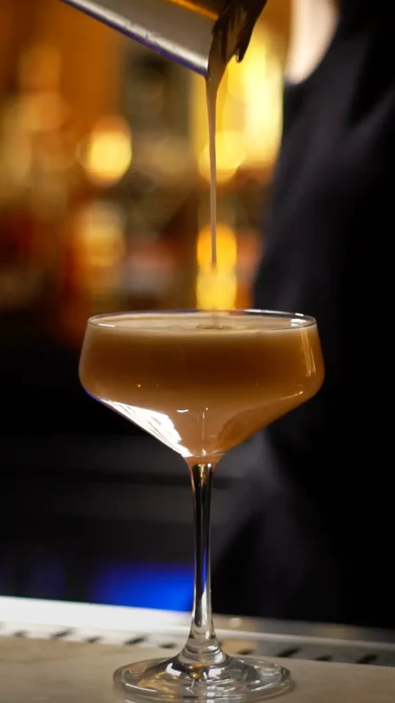 Bartender pouring a foamy cocktail into a glass.