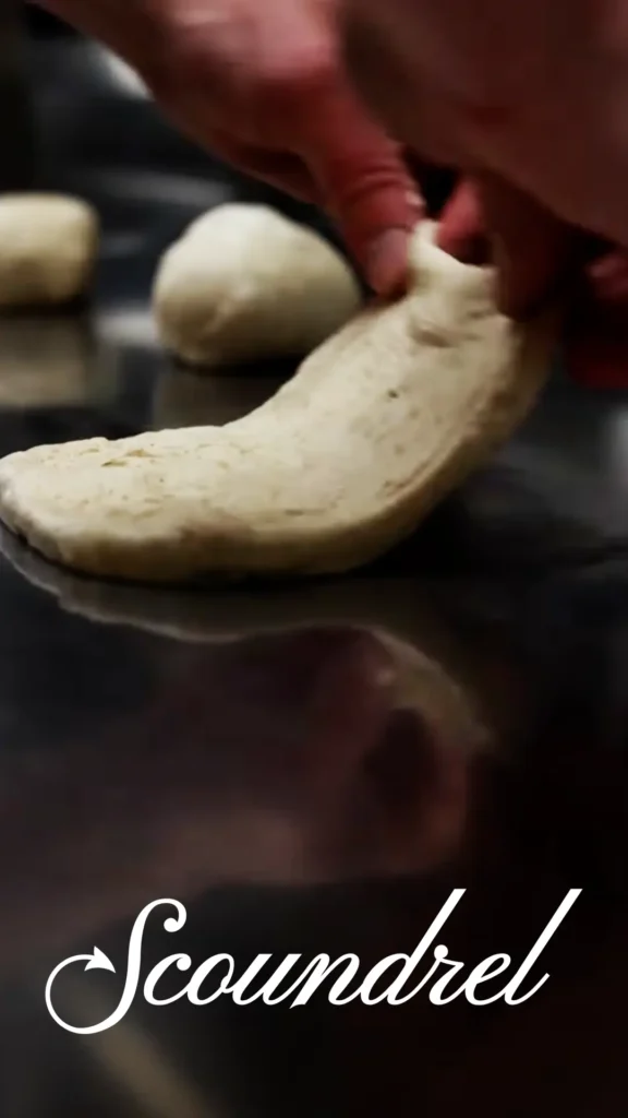 Baker kneads dough on a metal surface.